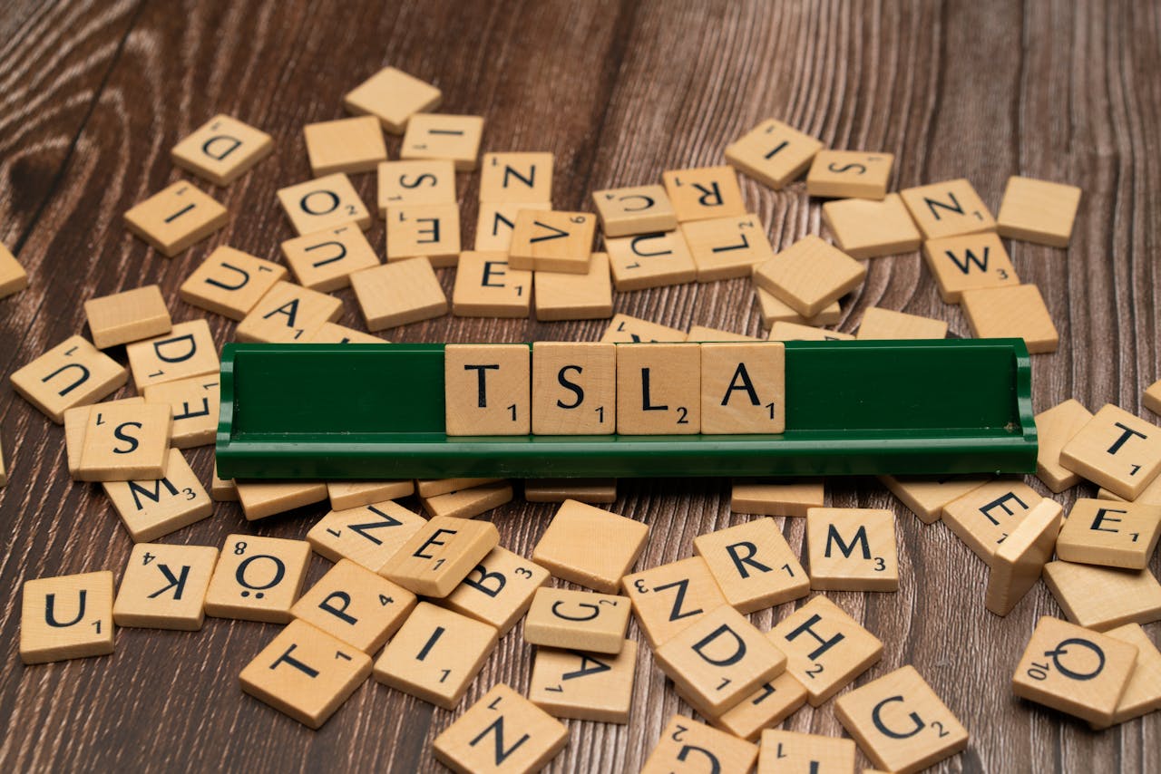 Wooden letter tiles spell TSLA, hinting at the stock market and investment themes.