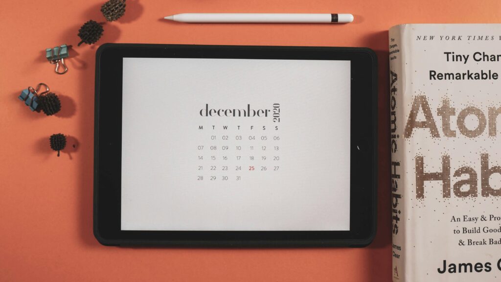 Minimalist flat lay featuring a tablet displaying a December 2020 calendar and a book.